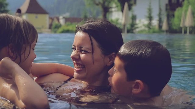 Happy mother hugging and kissing children inside warm pool in the mountain slow motion closeup