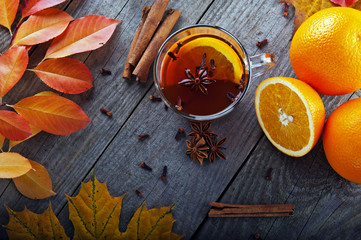 hot tea with spices and orange amid autumn leaves