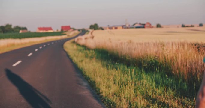 Traveler woman hitchhiking on a sunny road and walking. Young happy backpacker woman looking for a ride to start a journey on a sunlit country road. Slow motion, 120fps. 4K, DCi. Poland, Lower Silesia