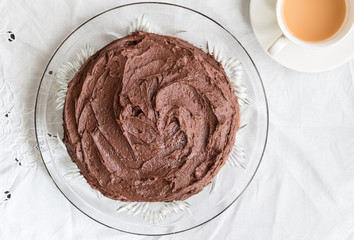 Rich creamy whole chocolate cake on white cloth with teacup - Top view photograph