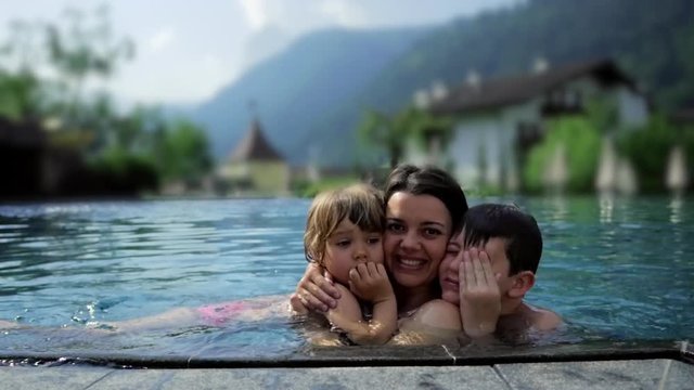 Happy mother hugging little daughter and boy inside warm pool in the mountain in vacation
