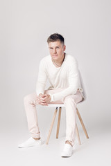 handsome young man in white sweater sits on a chair on 