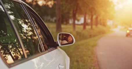 Woman showing legs from the car window and moving them playfully. Slow motion. Filmed in 4K DCi resolution. Young woman relaxing in the car during a stop on a road trip, with sunlit road background.