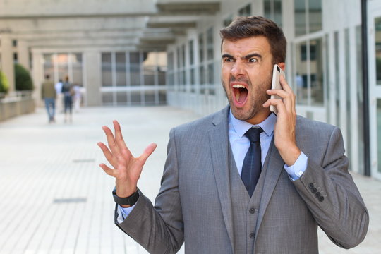 Desperate young brunette businessman get bad news heavy problems, faces challenges snort while talking on the mobile phone