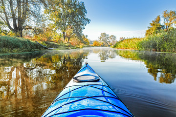 View from the blue kayak on the river banks with autumnal yellow leaves trees in fall season. The Seversky Donets river, autumn kayaking. View over nose of bright blue kayak.