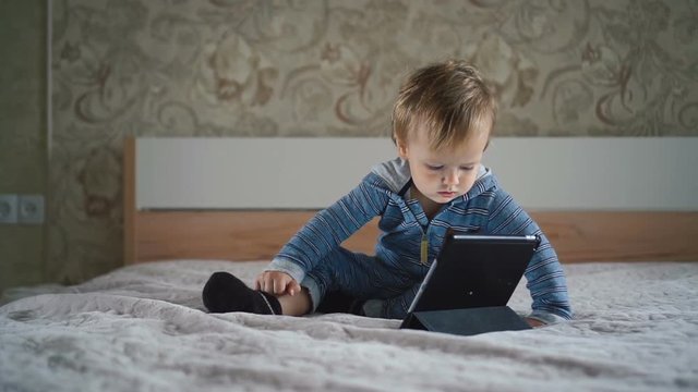 Little boy watching cartoons on digital tablet sitting on bed