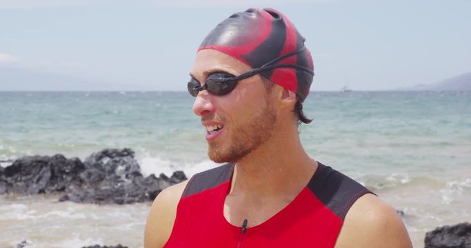 Triathlon swimming man - male triathlete swimmer taking off swim goggles ocean swim training session. Fit man in professional triathlon suit training for ironman on Hawaii.
