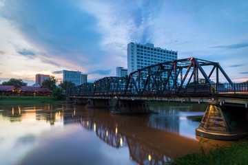 The historical iron bridge at Chiangmai city skyline at Ping river at dusk. Chiangmai , Thaland. Long exposure photograph.