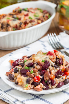 Baked rice casserole with black beans, pinto beans, kidney beans and cheese, on white plate, vertical