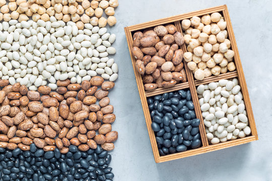 Different kinds of beans: black, pinto, white and chickpeas in wooden box and on concrete background, flat lay, horizontal