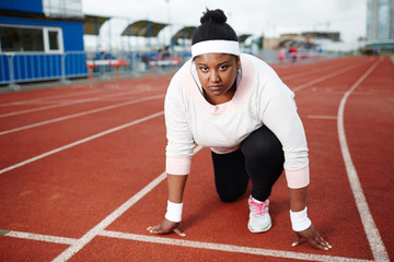 Young oversized competitor of marathon standing by line at low start on racetrack and waiting for...