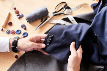 Fototapeta premium Close-up shot of talented young fashion designer working on male clothing collection while sitting at wooden table