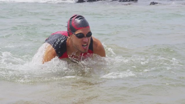 Triathlon swim. Male triathlete swimmer man running out of ocean after swimming finishing swimming. Fit man ending swimming sprinting out of water in professional triathlon suit training for ironman.
