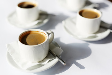 Three porcelain cups of black aromatic fresh hot coffee on white paper napkins and saucers