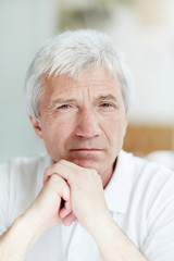 Calm man of retirement age staring at camera with his hands on chin