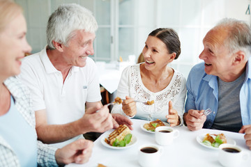 Obraz na płótnie Canvas Cheerful senior friends having tasty dessert and talking in cafe