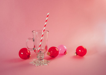 Christmas trendy pink composition with red transparent glass baubles, peppermint swirl candy, mulled vine glass with striped paper straw