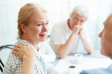 Crying senior female listening to her friend supporting her in grief