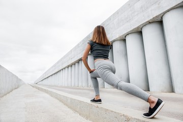 Beautiful woman doing workout on the street against concrete walls