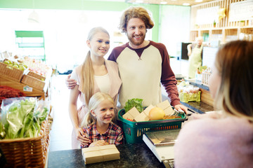 Happy couple and ther daughter standing by cash desk and looking at cashier