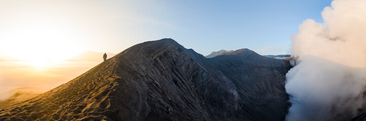 An adult man is seen from behind, walking on a sand path along the central crater of Mount Bromo...