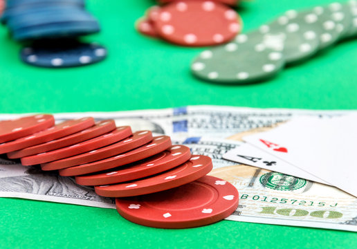 Poker chips with money and two aces on the green poker table.
