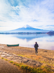 Fototapeta premium silhouette asia girl traveler 30s to 40s stand and walk to lake with boat on ground at side of lake kawaguchi on morning time with fuji mountain background