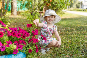 Fototapeta premium 6-year-old girl sitting near flowers petunias