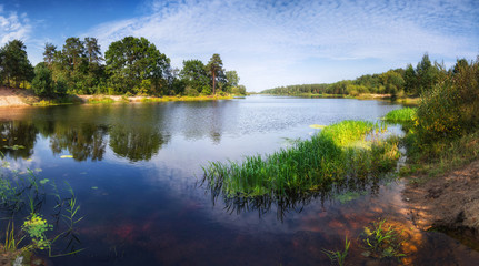Beautiful landscape of the lake at sunny day. Panoramic view of the backwater and green coast with trees reflecting in the water. 