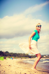 Blonde woman wearing dress playing jumping on beach