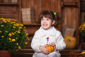 Fototapeta premium Portrait of adorable smiling girl posing with orange pumpkin in fall wooden interior.