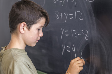 Schoolboy solving a problem on a blackboard.