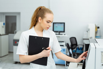 Attractive female lab worker making medical research in modern laboratory. Scientist holding documents folder with analysis results.