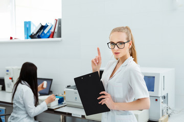 Attractive female lab worker making medical research in modern laboratory. Scientist holding...