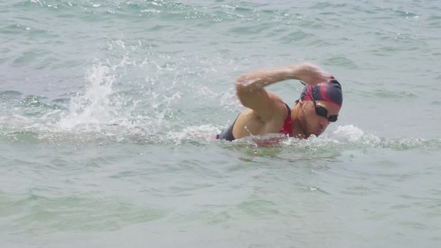 Triathlete man swimming freestyle crawl in ocean. Male triathlon swimmer swimming in professional triathlon suit training for ironman.