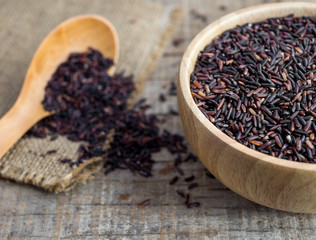 Close up rice berry(brown rice, Thai black jasmine rice or raw purple/red rice) in a wooden bowl, spoon and sack on wooden background.