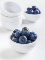 Freschi mirtilli con ciotoline su sfondo bianco