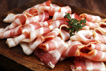 Raw sliced bacon with thyme leaves ready for cooking.