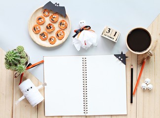 Halloween, celebration or holiday background concept : Mock up of open notebook, paper crafts, cube calendar, grilled carrots with scary face and coffee cup, Top view or flat lay with copy space