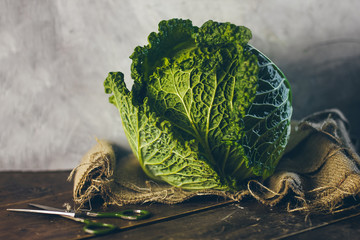 A fresh green savoy cabbage on the sackcloth on the wooden table with the scissors near by