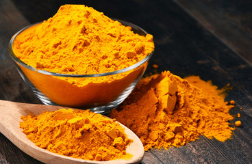 Composition with bowl of turmeric powder on wooden table
