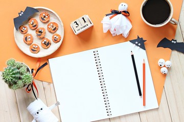 Halloween, celebration or holiday background concept : Mock up of open notebook, paper crafts, cube calendar, grilled carrots with scary face and coffee cup, Top view or flat lay with copy space