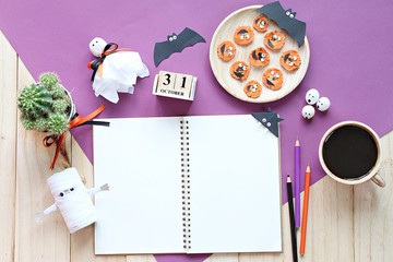 Halloween, celebration or holiday background concept : Mock up of open notebook, paper crafts, cube calendar, grilled carrots with scary face and coffee cup, Top view or flat lay with copy space