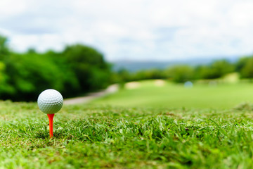 close up of white golf ball on orange tee on green grass with blue sky and cloud. copy space for your text.