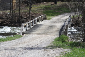 Wooden bridge spanning a fast moving creek full of water. 