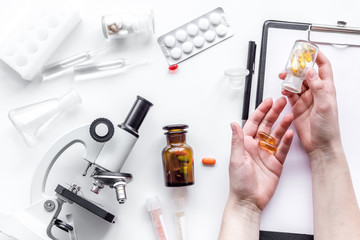 Do medcal tests. Hands hold pills near microscope on white background top view