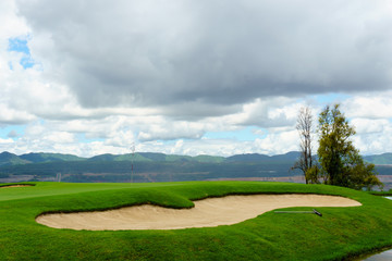 beautiful idyllic view green with sand trap and white flag and view of mountain, blue sky with clouds