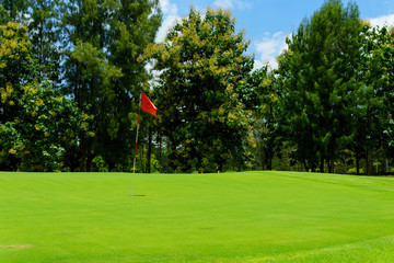 Obraz premium beautiful idyllic view of green with red flag and view of forest, blue sky with clouds.