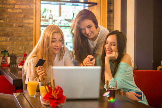 Three teenage girls shopping online together in a cafe.