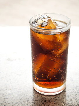 Black soft drink in glass with ice cube. On marble floor. Favorite soft drink for refreshment. Side view. 